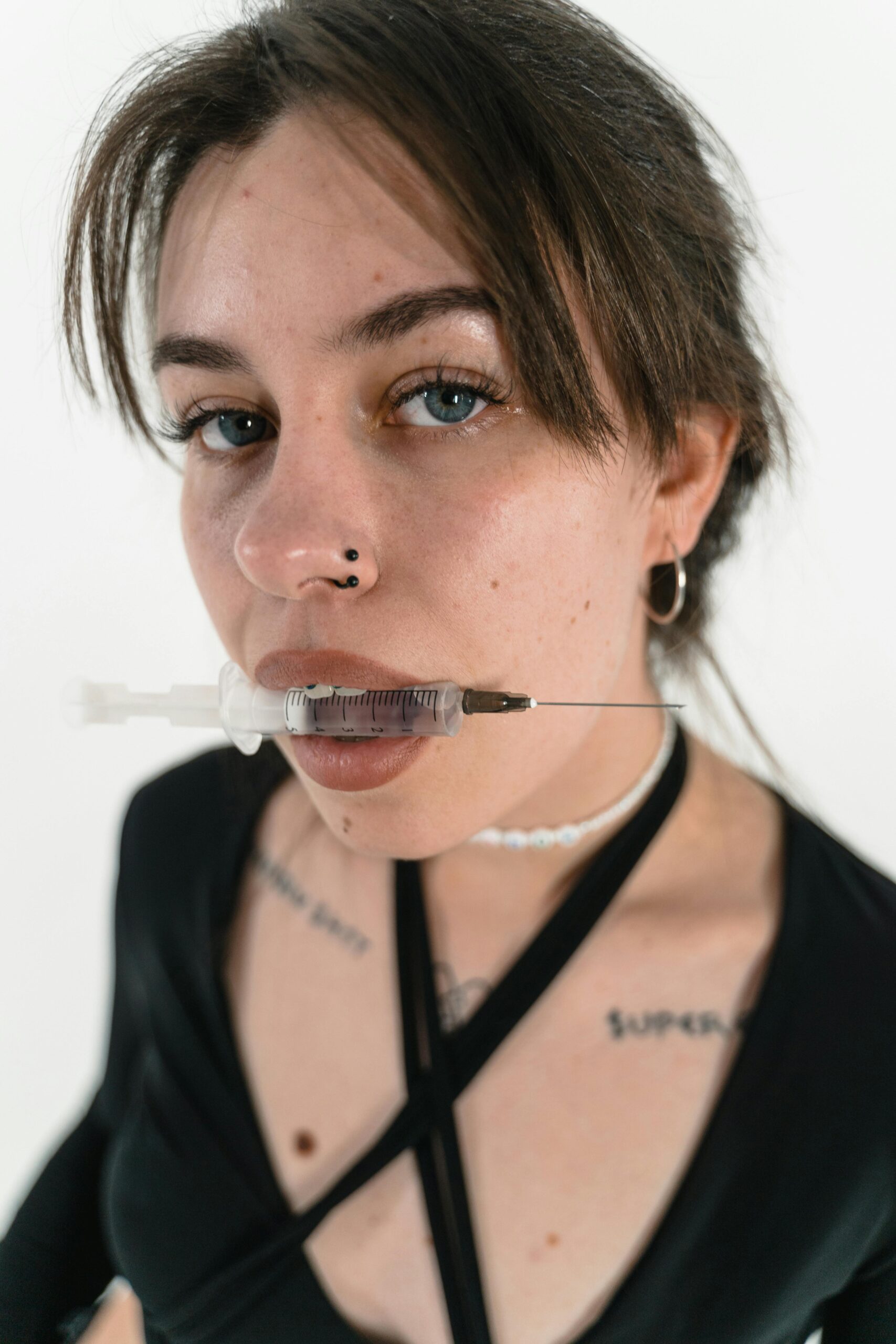 Close-up portrait of a woman holding a syringe in her mouth, conveying conceptual themes.