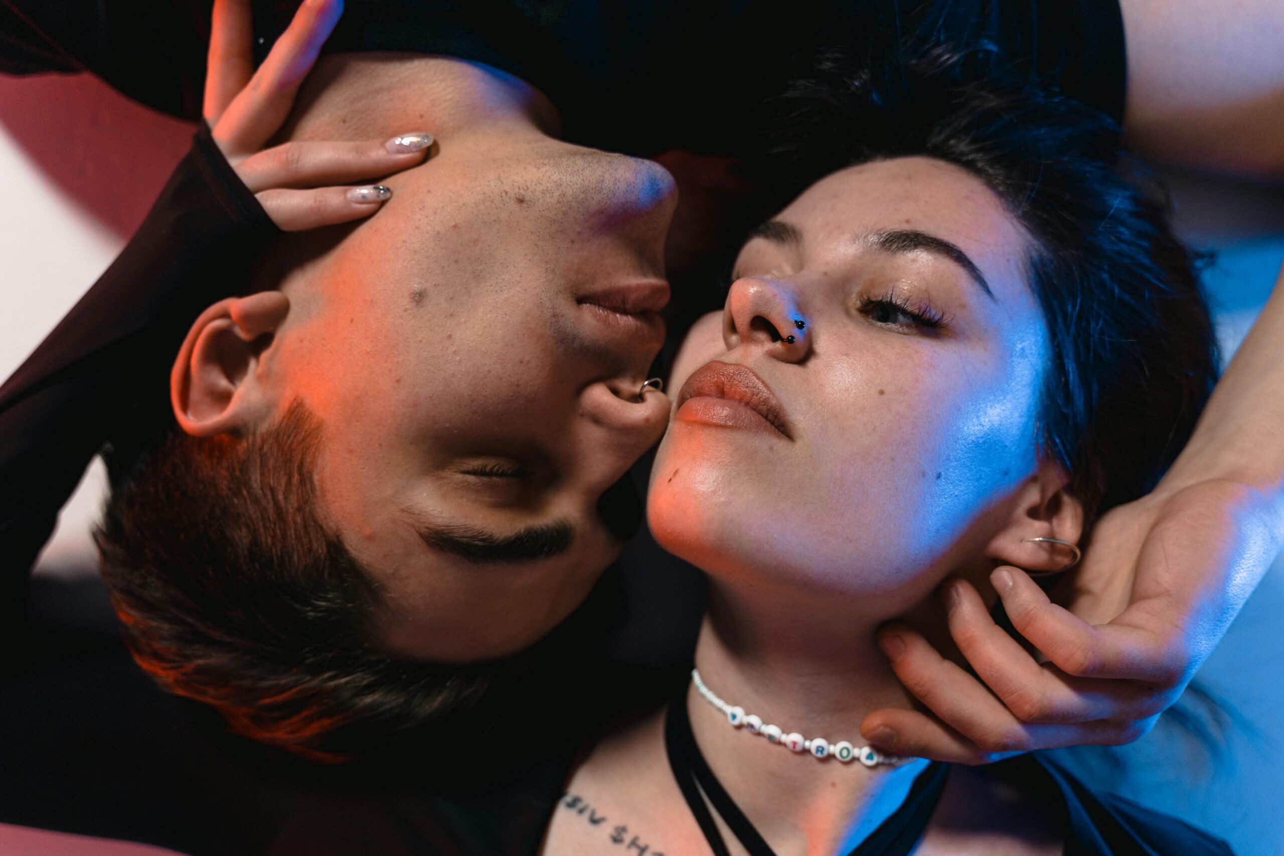 Close-up of an intimate couple under vibrant red and blue lighting, expressing connection and emotion.